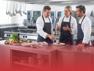 Equipo de chefs profesionales participando en capacitación gastronómica práctica en cocina industrial moderna para la industria alimentaria.